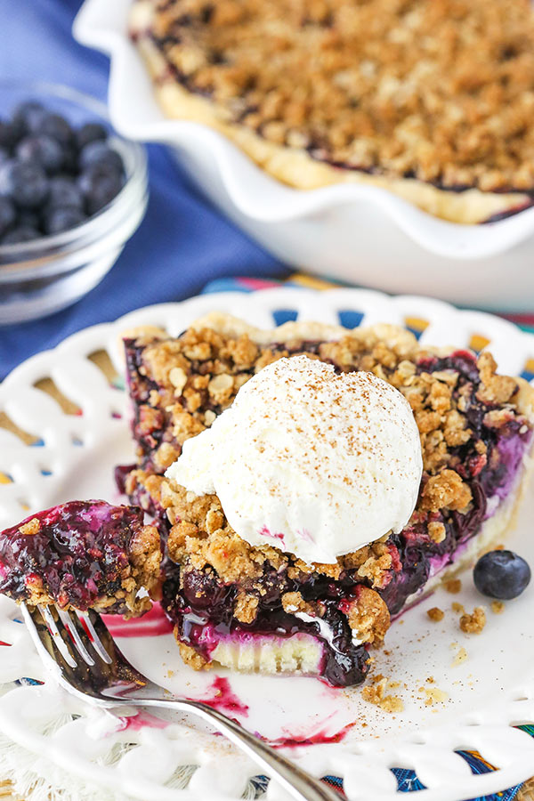 A slice of Blueberry Crumb Cheesecake Pie on a white plate with a bite removed. 