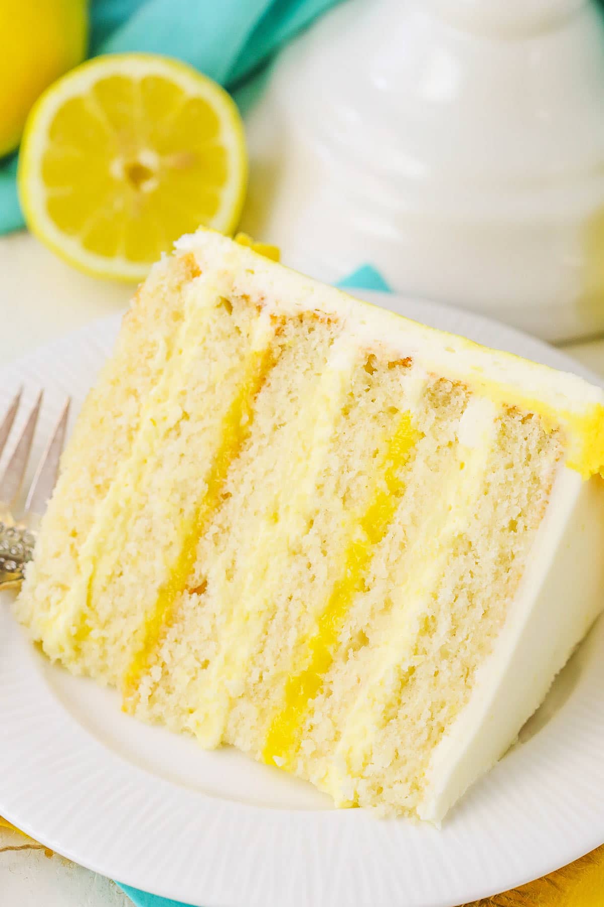 A Big Slice of Summer Citrus Cake on a White Plate with Half a Lemon Behind it