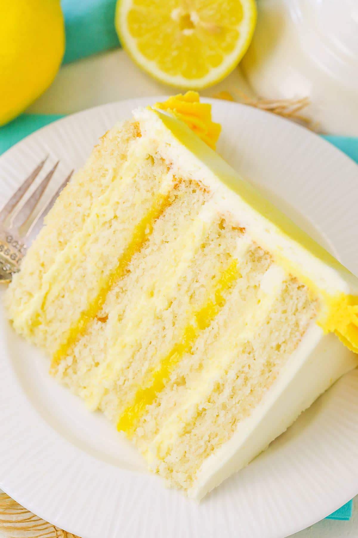 A Piece of Lemon Layer Cake on a White Dessert Plate with a Metal Fork