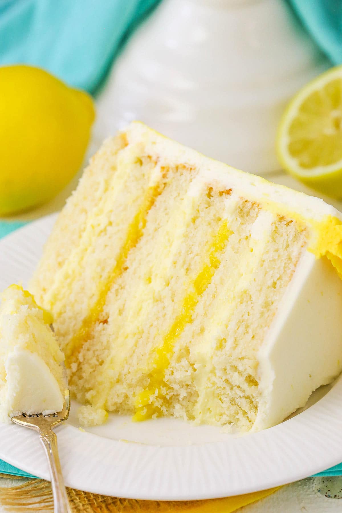 A Partially Eaten Piece of Lemon Layer Cake on a Plate with One Bite on a Fork