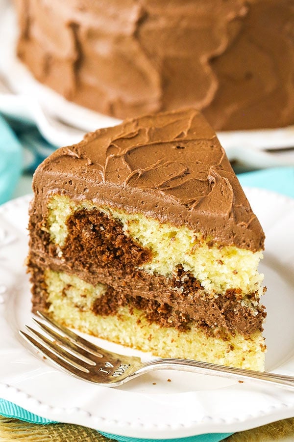 A slice of frosted marble cake with swirls of vanilla and chocolate cake visible
