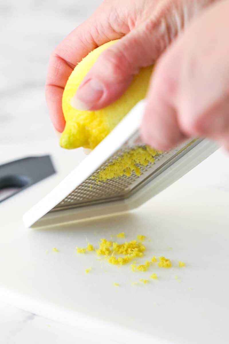 zesting a lemon on a zester over a white cutting board