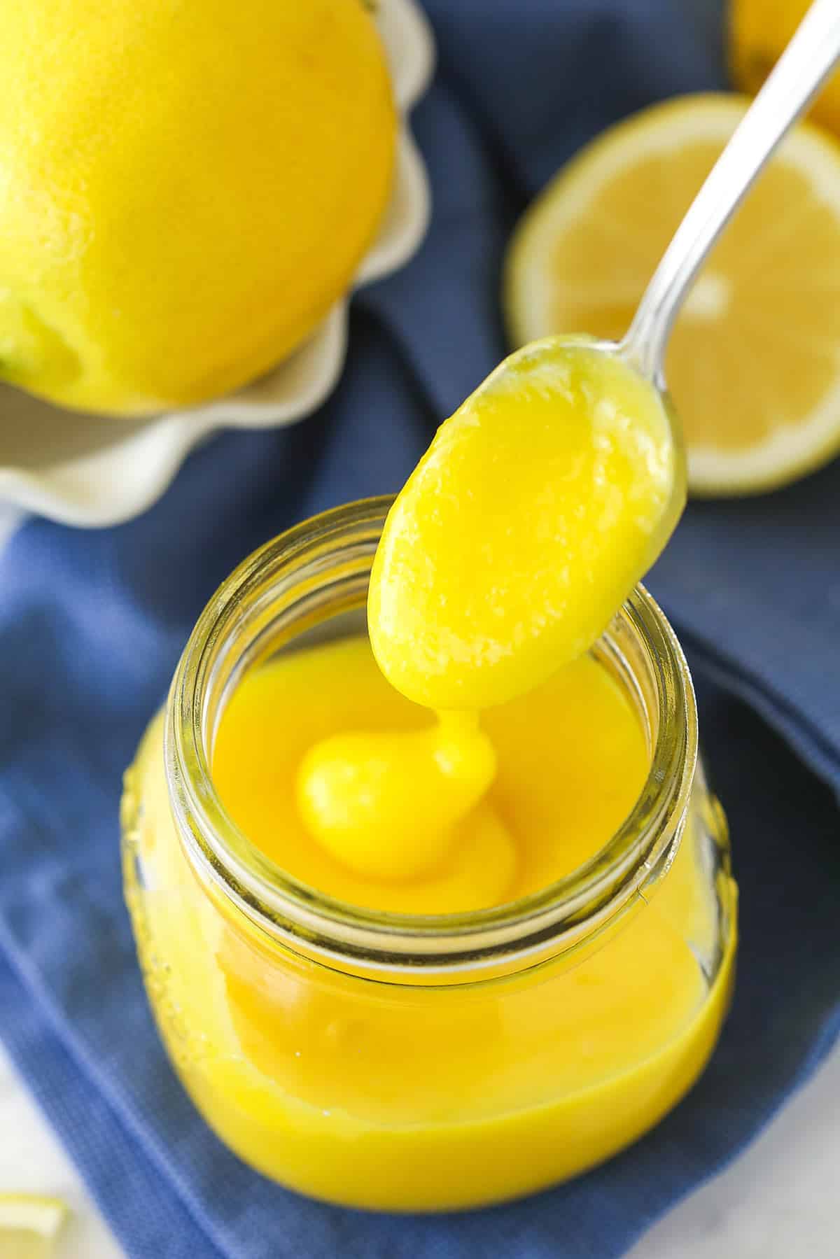 overhead image of lemon curd being drizzled into clear jar with a spoon