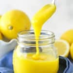 lemon curd being drizzled into clear jar with a spoon