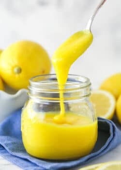 lemon curd being drizzled into clear jar with a spoon
