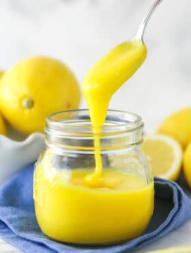 lemon curd being drizzled into clear jar with a spoon