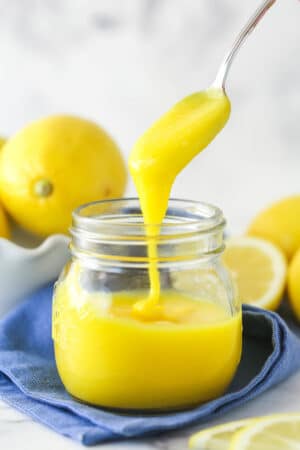 lemon curd being drizzled into clear jar with a spoon