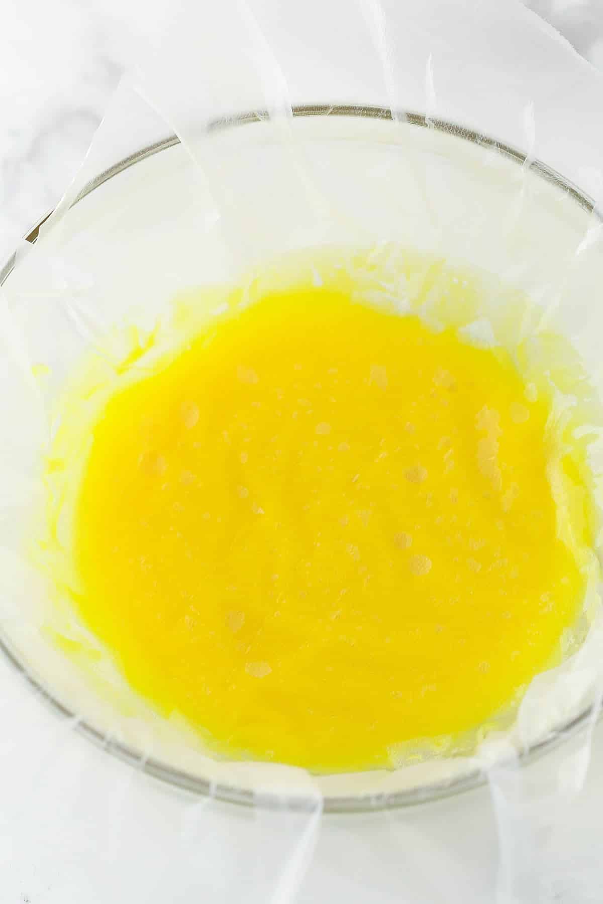 cooked lemon curd in clear bowl with clear wrap pressed on top