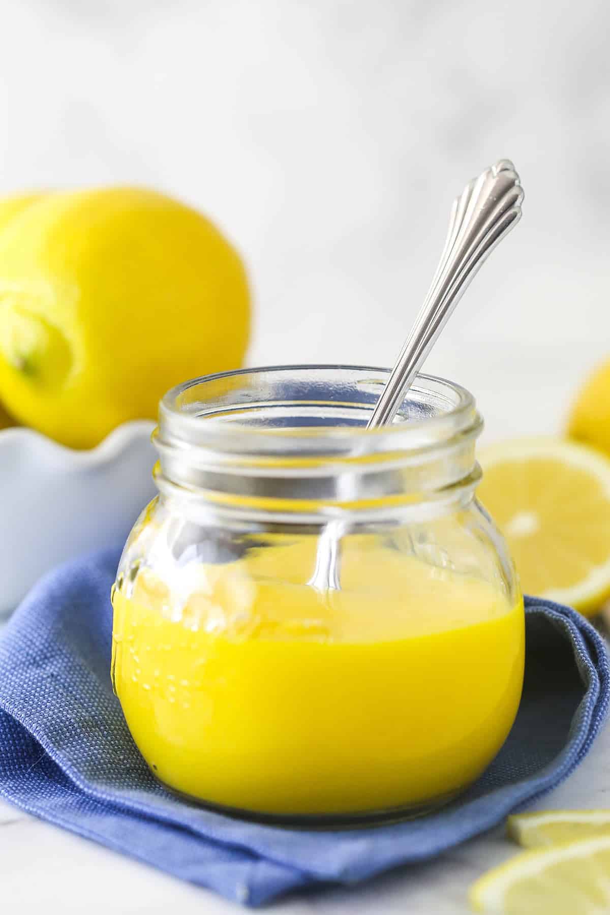 lemon curd in glass jar with blue cloth and spoon in it