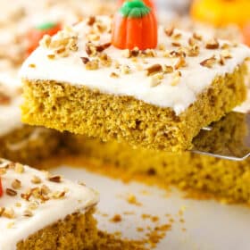 Slice of frosted pumpkin sheet cake being lifted from a sheet pan with a spatula.