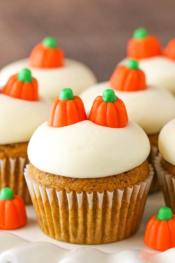 A pumpkin cupcake with cream cheese frosting and two candy pumpkins on top