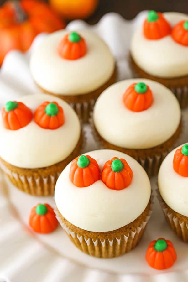 A white serving tray full of pumpkin cupcakes with one or two mellowcreme pumpkins on top