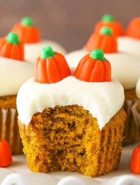 A frosted pumpkin cupcake on a serving platter with a big bite taken out of it
