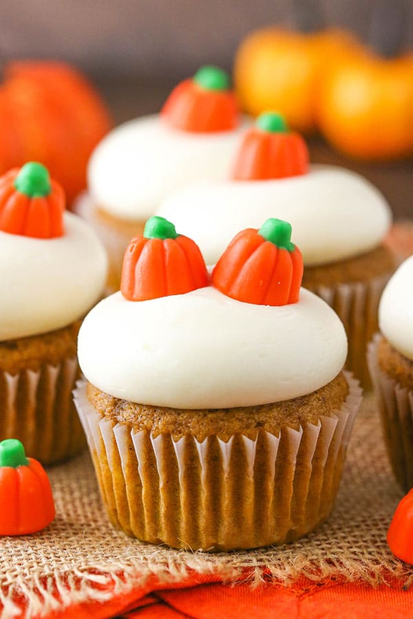 A close-up shot of a pumpkin cupcake on a table with pumpkins and more cupcakes in the background
