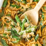 A baking dish full of green bean casserole with a wooden spoon digging in