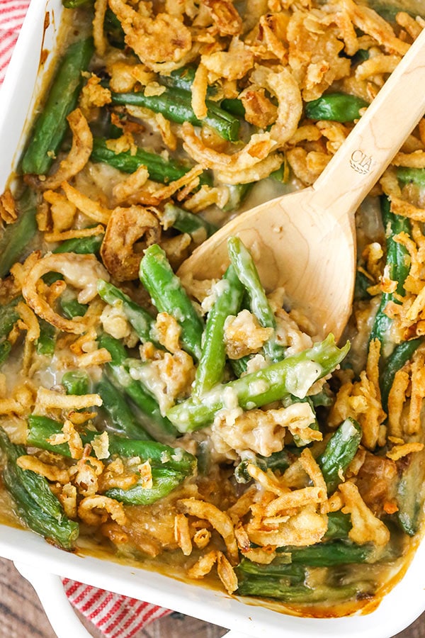 A baking dish full of green bean casserole with a wooden spoon digging in