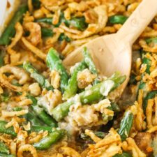 A wooden spoon scooping up a serving of green bean casserole from a ceramic baking dish.