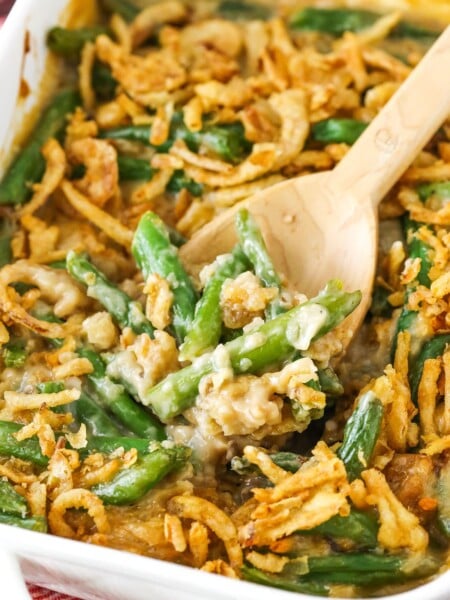 A wooden spoon scooping up a serving of green bean casserole from a ceramic baking dish.