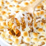 A wooden spoon scooping out a helping of sweet potato casserole from a white baking dish