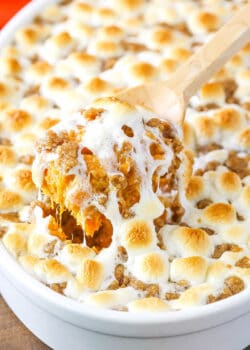 Sweet Potato Casserole with marshmallows in a white dish with a scoop being taken out