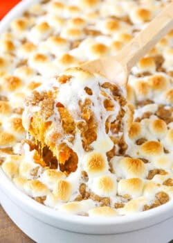 A wooden spoon scooping out a helping of sweet potato casserole from a white baking dish