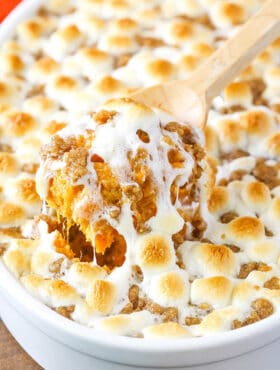 A wooden spoon scooping out a helping of sweet potato casserole from a white baking dish