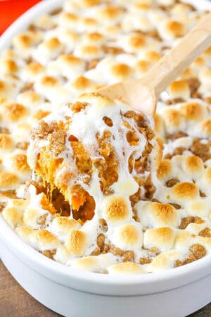 A wooden spoon scooping out a helping of sweet potato casserole from a white baking dish