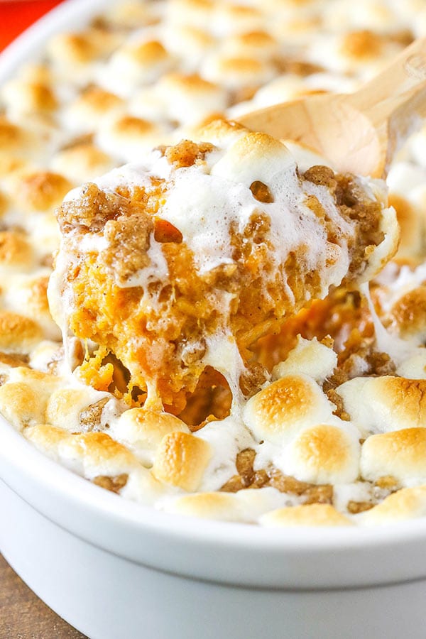 Close up of Sweet Potato Casserole with marshmallows in a white dish and a scoop being removed 