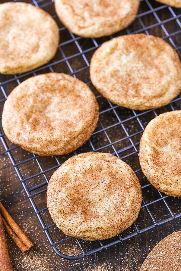 Homemade snickerdoodles cooling on a metal rack beside a bowl of cinnamon sugar