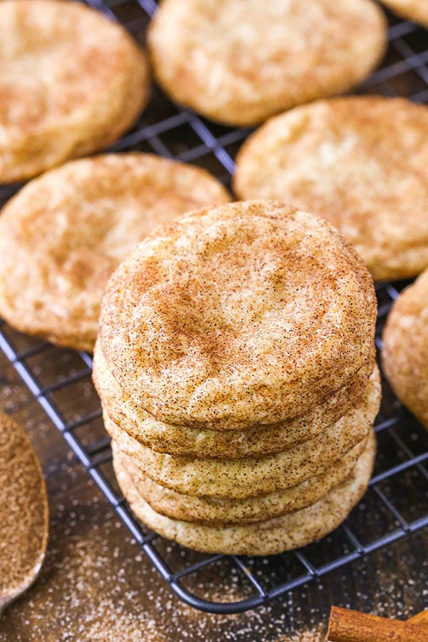 A stack of five snickerdoodle cookies on a cooling rack with singular cookies lined up behind the stack