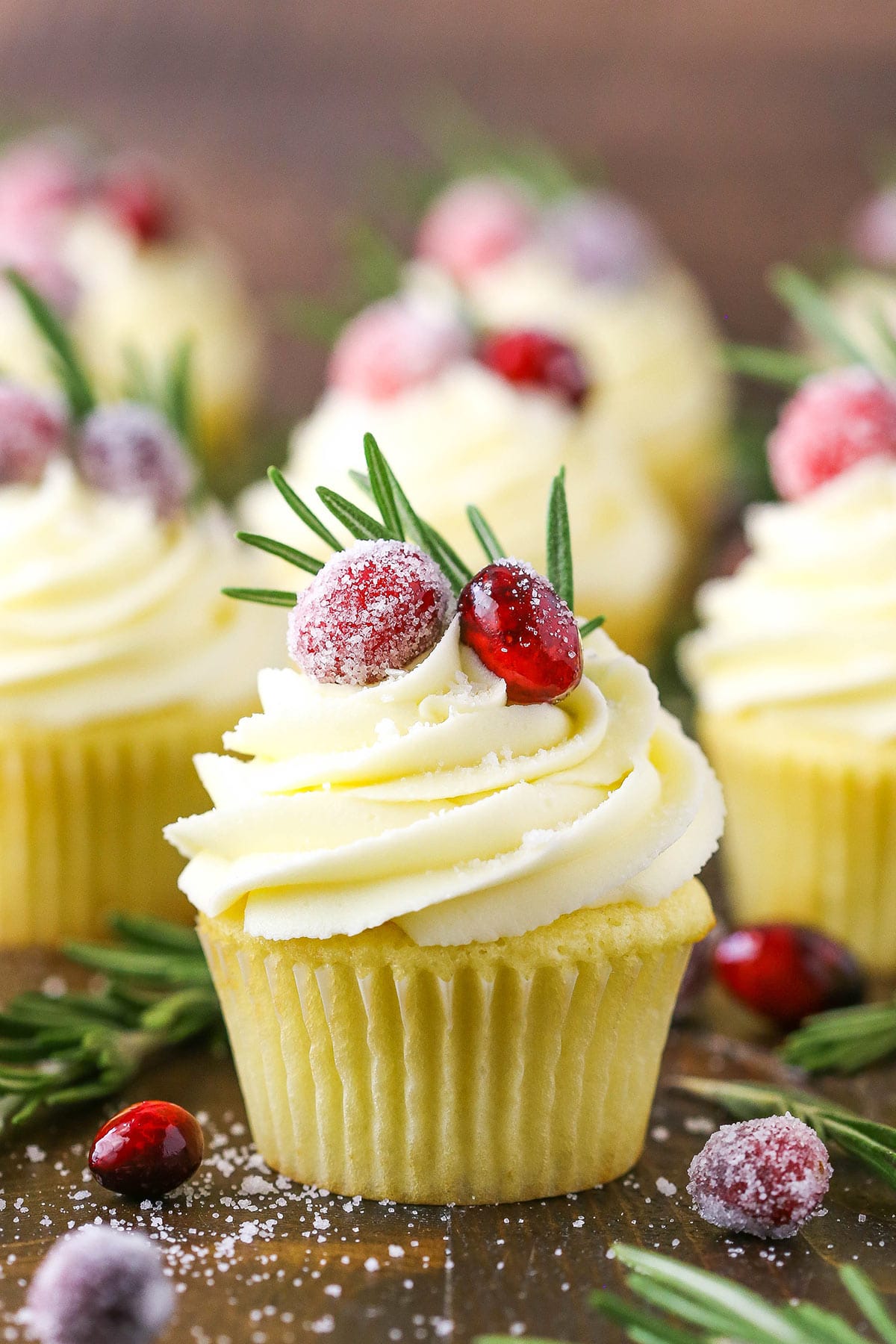 A sparkling cranberry white chocolate cupcake on a wooden table with more cupcakes behind it