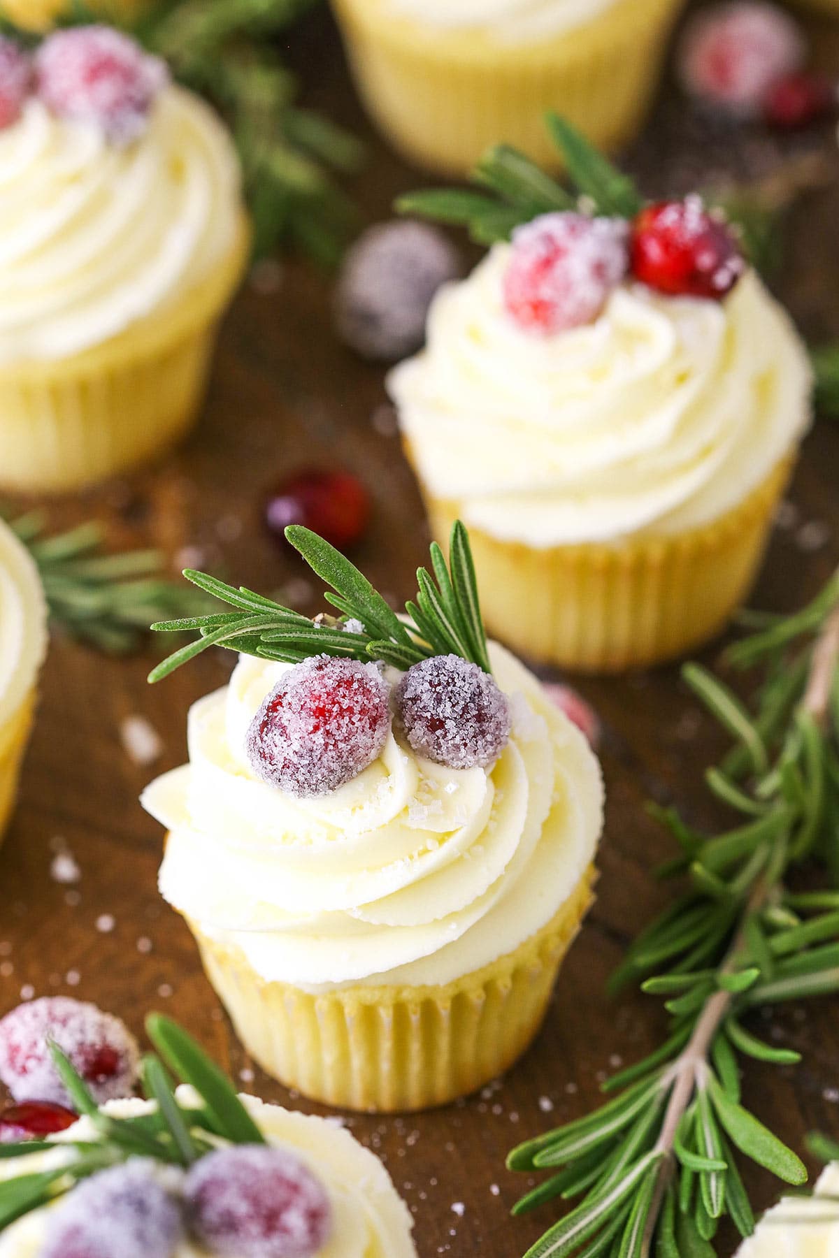 White chocolate cranberry cupcakes on a dining table with sprigs of fresh rosemary