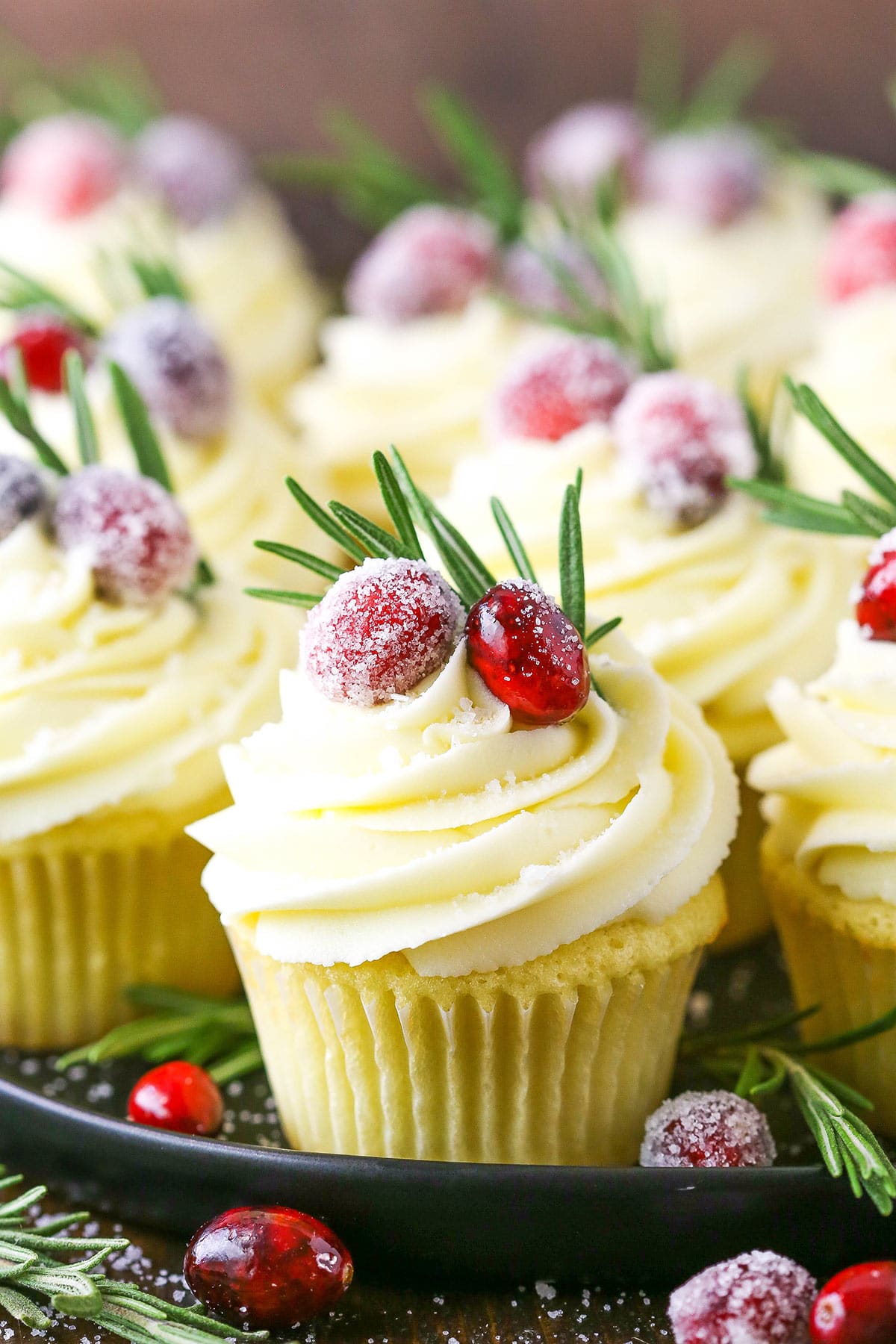A serving platter full of cranberry white chocolate cupcakes garnished with sparkling cranberries and rosemary