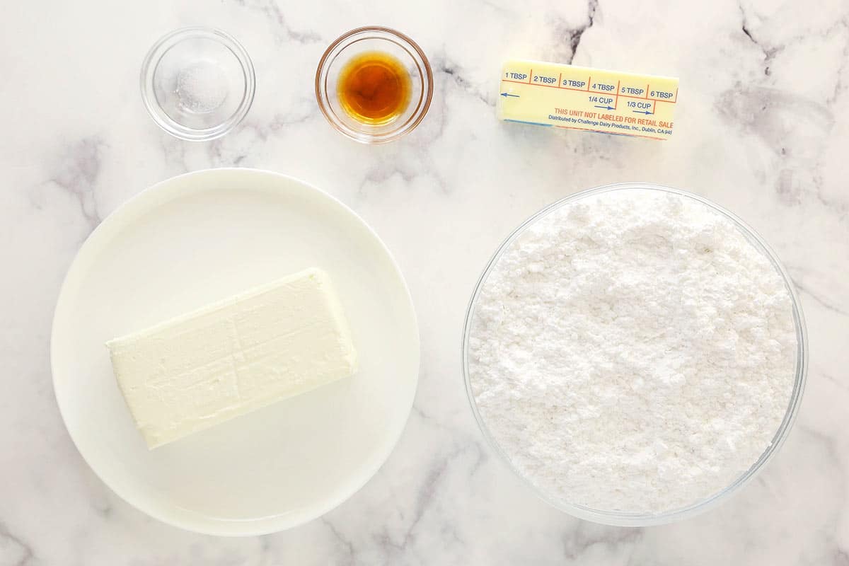 This Cream Cheese Frosting is perfect for topping cupcakes and frosting cakes! It pipes beautifully and holds it's shape, it's perfectly sweet and tangy and it's easy to make with just 5 ingredients. salt, vanilla, butter, cream cheese and powdered sugar in glass bowls on marble table