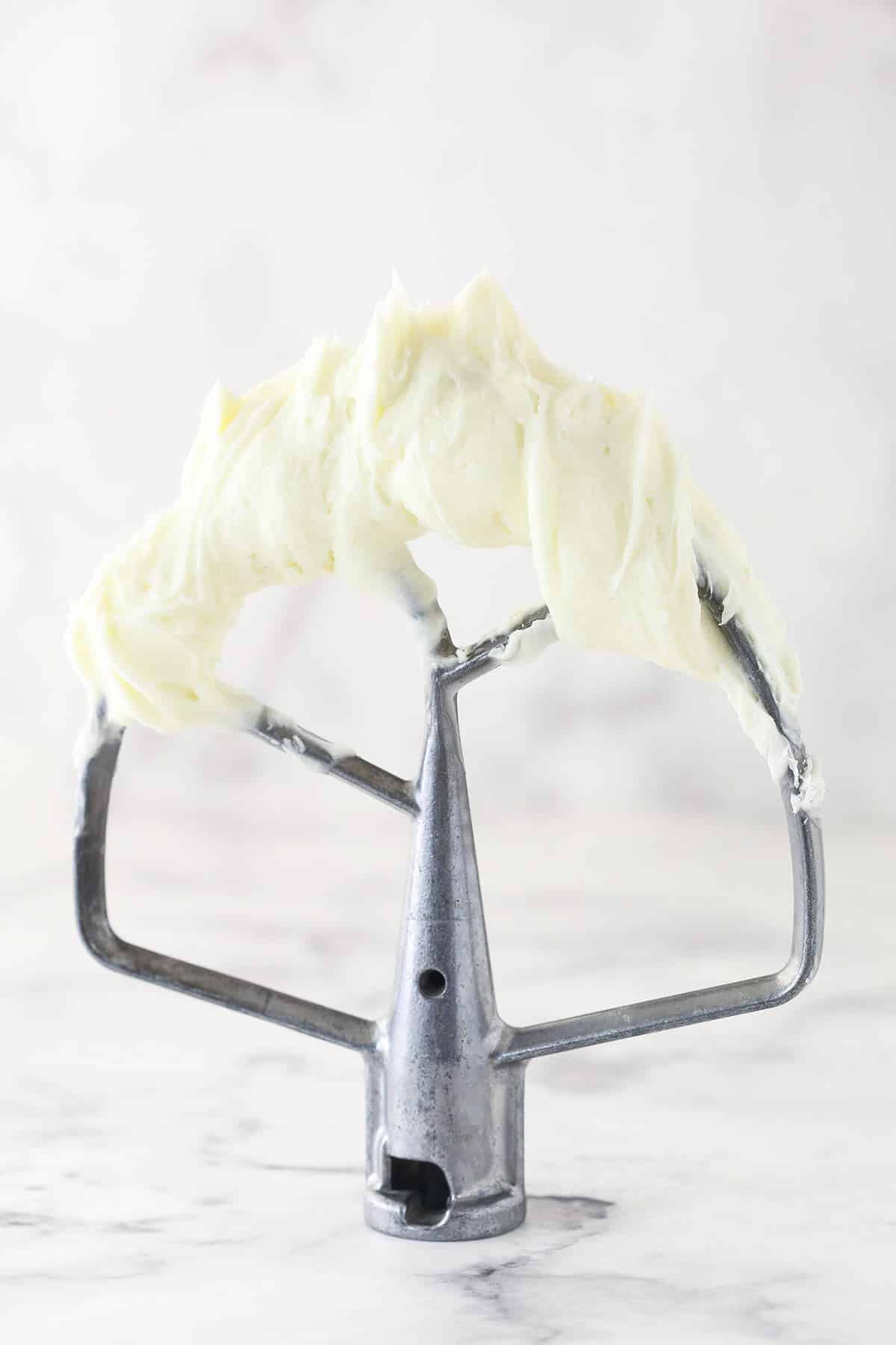 cream cheese frosting on metal mixer blade standing on marble table