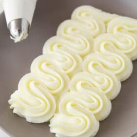 cream cheese frosting piped onto gray plate with piping bag in the corner