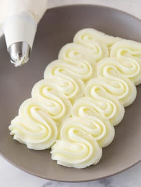 cream cheese frosting piped onto gray plate with piping bag in the corner