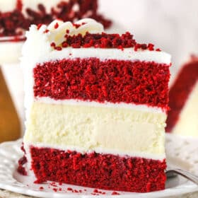 piece of red velvet cheesecake cake siting upright on white plate, cream napkin and marble table