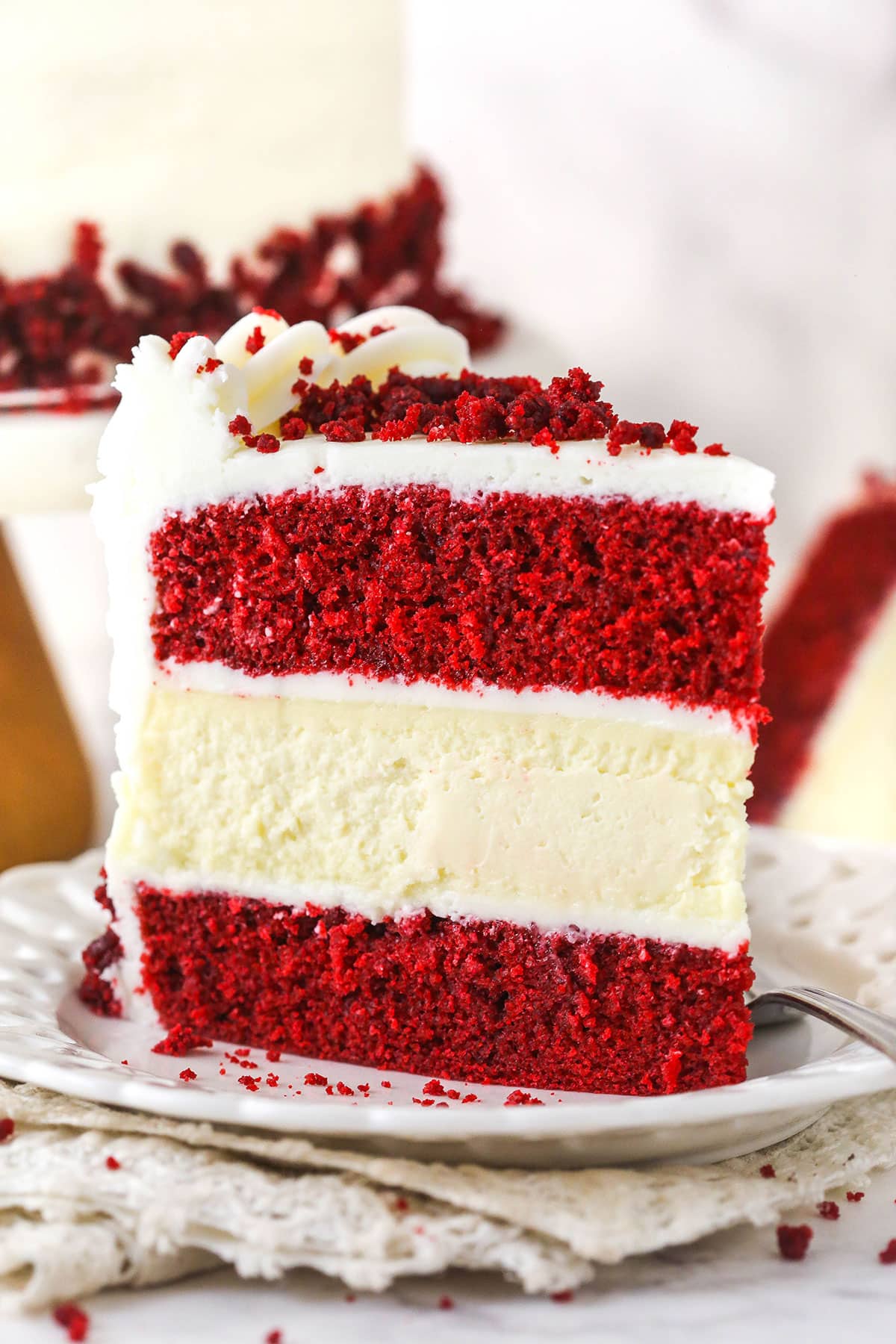 piece of red velvet cheesecake cake siting upright on white plate, cream napkin and marble table