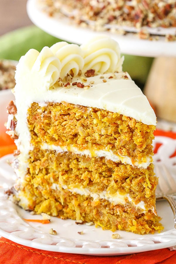 A big slice of carrot cake with decorative cream cheese frosting on a white plate