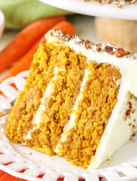 A slice of homemade carrot cake with cream cheese frosting on a white plate