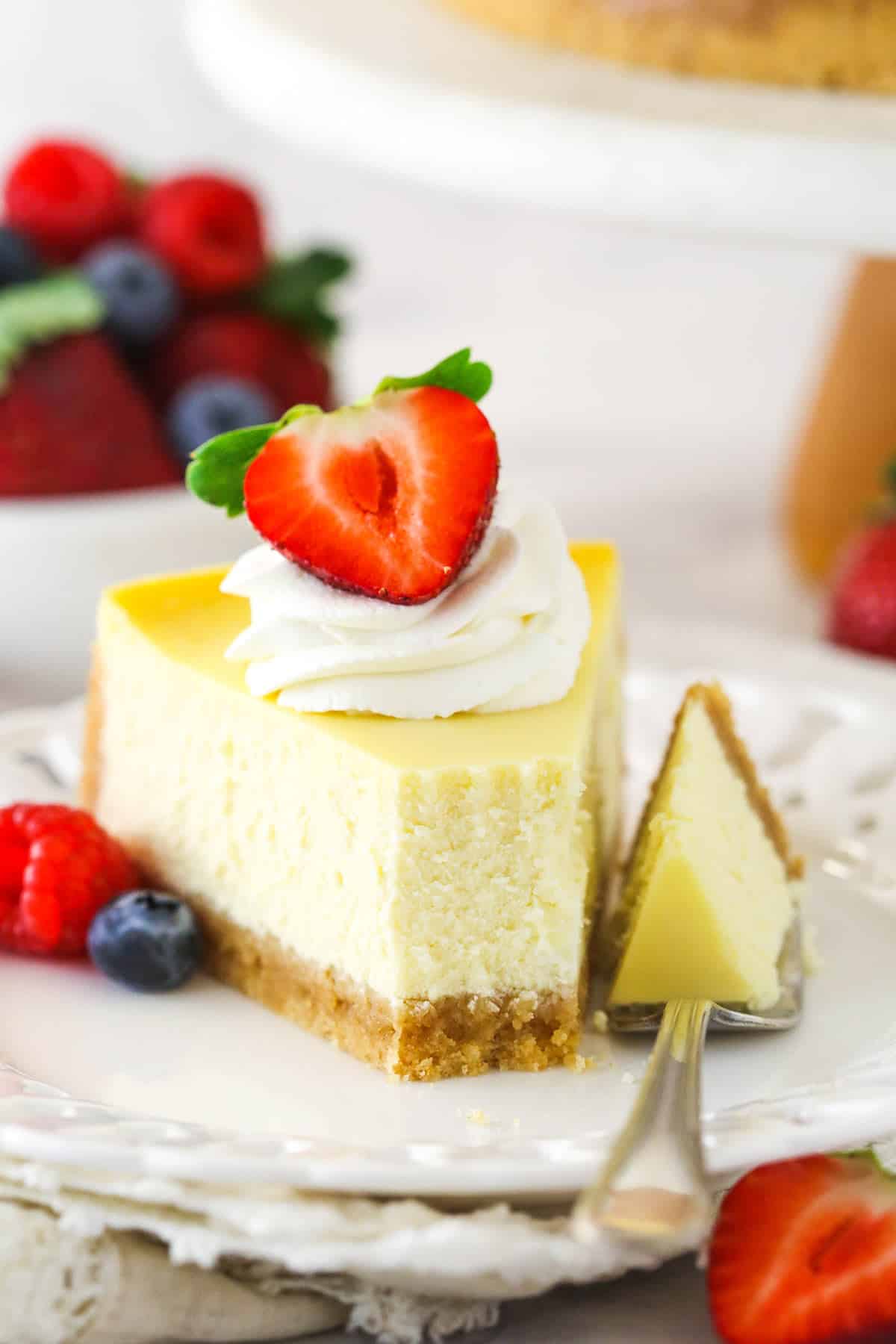A slice of homemade cheesecake with whipped cream and berries with a bite taken