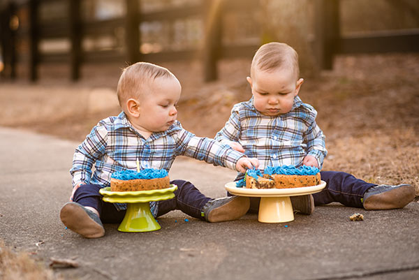 the twins sitting on the floor eating a cookie cake