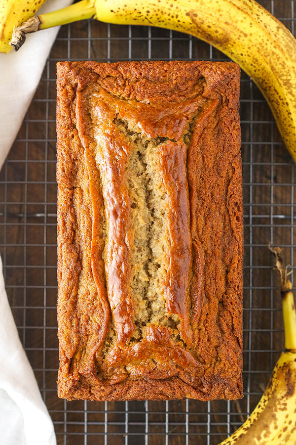 Fresh loaf of banana bread on a cooling rack with bananas