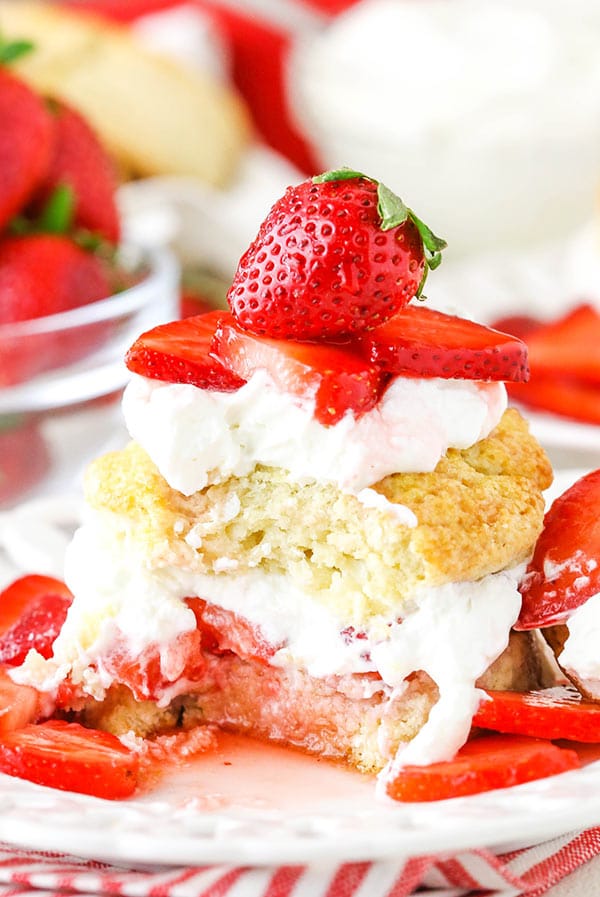 Shortcake biscuit filled with homemade whipped cream and topped with strawberries with a bite taken out.