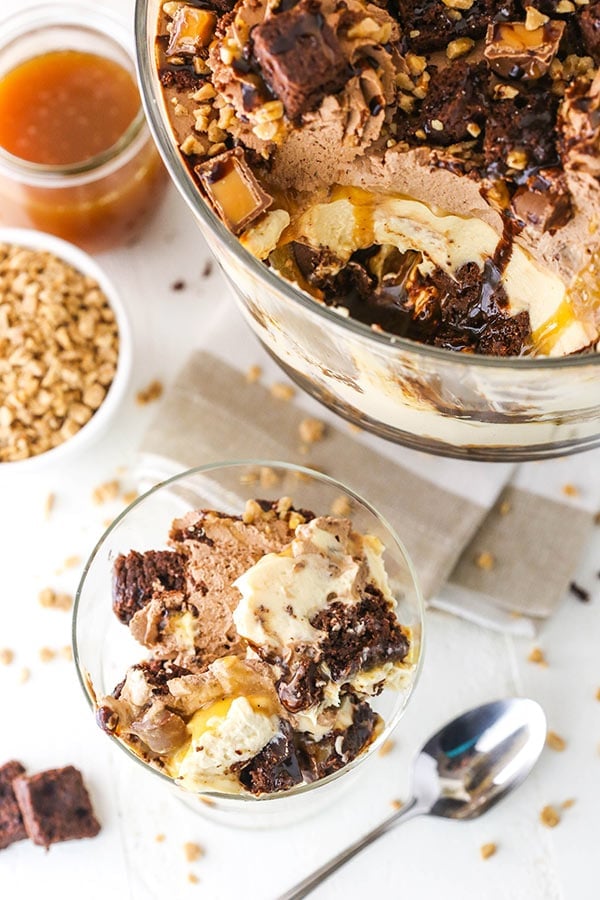 A serving of caramel cheesecake brownie trifle in a small parfait dish with the full trifle beside it