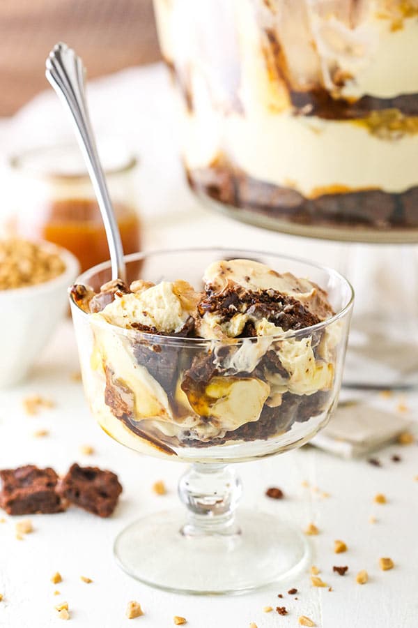 A helping of caramel cheesecake brownie trifle in a glass with a metal dessert spoon inside