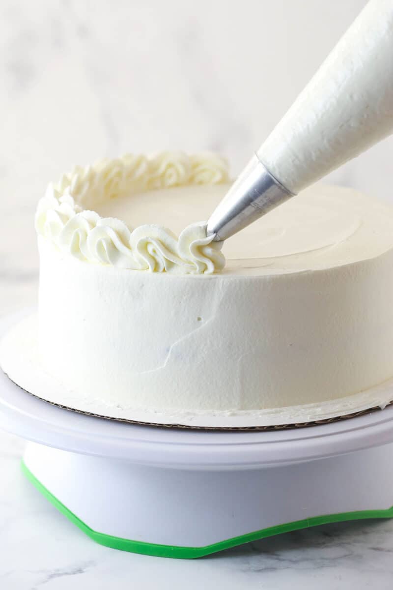 Decorating an ice cream cake with a pipping bag and whipped cream.