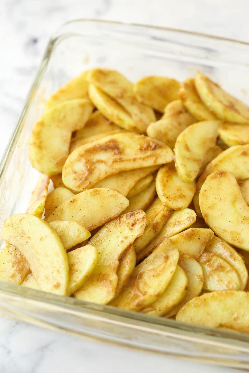 sliced apples tossed with sugar and spices in glass baking dish