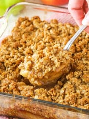 An apple crisp in a glass baking dish with a serving spoon removing a heaping section from the middle